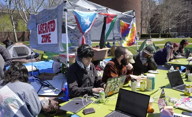 A Massachusetts Institute of Technology student, center, does school work on his computer while seated with others, Monday, April 22, 2024, at an encampment of tents on the MIT campus, in Cambridge, Mass. Students at MIT set up the encampment to protest what they said was MIT's failure to call for an immediate ceasefire in Gaza and to cut ties to Israel's military. (AP Photo/Steven Senne)