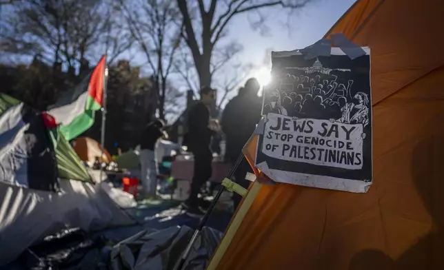 Students protesting against the war in Gaza stand next to a Palestinian flag and tents at an encampment in Harvard Yard, at Harvard University in Cambridge, Mass., on Thursday, April 25, 2024. (AP Photo/Ben Curtis)