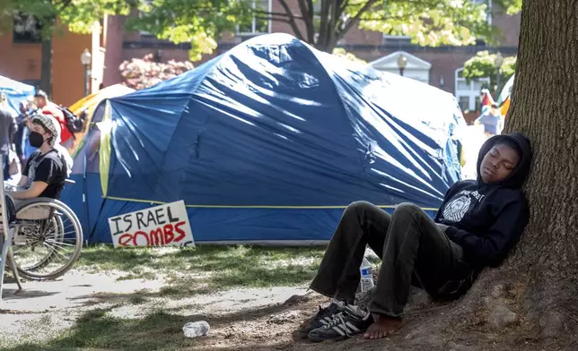 A person rests against a tree at an encampment by students protesting against the Israel-Hamas war at George Washington University on Monday, April 29, 2024, in Washington. (AP Photo/Mark Schiefelbein)