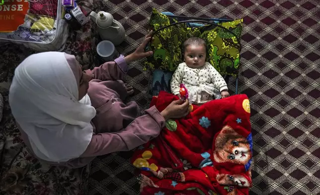 Rola Saqer sits beside her baby Massa Mohammad Zaqout in her parents' home in Nuseirat refugee camp, central Gaza, Thursday, April 4, 2024. Zaqout was born Oct. 7, the day the Israel-Hamas war erupted. Mothers who gave birth in the Gaza Strip that day fret that their 6-month-old babies have known nothing but brutal war, characterized by a lack of baby food, unsanitary shelter conditions and the crashing of airstrikes. (AP Photo/Abdel Kareem Hana)