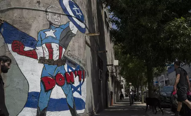 A man walks past a mural depicting the U.S. president Joe Biden as a superhero defending Israel on a street in Tel Aviv, Israel, Sunday, April 14, 2024. Israel on Sunday hailed its successful air defenses in the face of an unprecedented attack by Iran, saying it and its allies thwarted 99% of the more than 300 drones and missiles launched toward its territory. But regional tensions remain high, amid fears of further escalation in the event of a possible Israeli counter-strike. (AP Photo/Leo Correa)