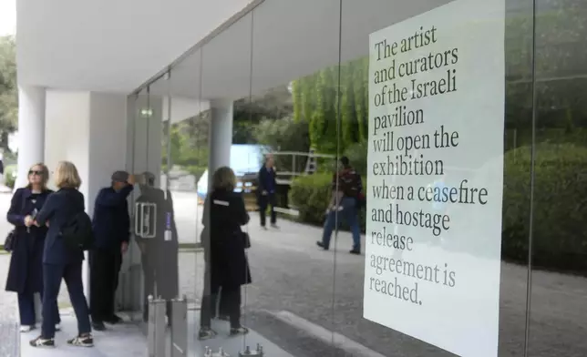 People stand in front of the closed Israeli national pavilion at the Biennale contemporary art fair in Venice, Italy, Tuesday, April 16, 2024 The sign at right announced that the artist and curators representing Israel at this year's Venice Biennale won't open the Israeli pavilion until there is a cease-fire in Gaza and an agreement to release hostages taken Oct. 7.(AP Photo/Luca Bruno)
