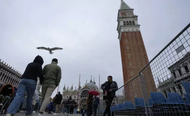People walk next to seats placed ahead of Pope Francis' visit on Sunday in St. Mark Square, in Venice, Italy, Saturday, April 27, 2024. (AP Photo/Antonio Calanni)