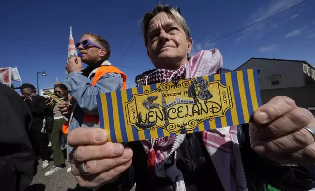 A citizen shows a ticket with the writing 'Veniceland' during a protest against Venice Tax Fee in Venice, Italy, Thursday, April 25, 2024. The fragile lagoon city of Venice begins a pilot program Thursday to charge daytrippers a 5 euro entry fee that authorities hope will discourage tourists from arriving on peak days. The daytripper tax is being tested on 29 days through July, mostly weekends and holidays starting with Italy's Liberation Day holiday Thursday. Officials expect some 10,000 people will pay the fee to access the city on the first day, downloading a QR code to prove their payment, while another 70,000 will receive exceptions, for example, because they work in Venice or live in the Veneto region. (AP Photo/Luca Bruno)