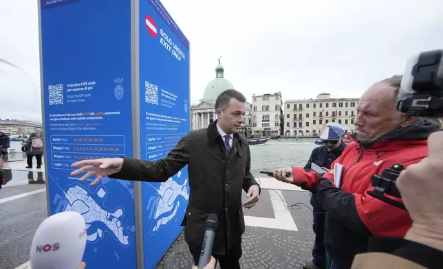 Venice councillor Simone Venturini speaks with reporters in front of a tourist tax totem in Venice, Italy, Wednesday, April 24, 2024. The lagoon city of Venice begins a pilot program Thursday, April 25, 2024 to charge daytrippers a 5 euro entry fee that authorities hope will discourage tourists from arriving on peak days. Officials expect some 10,000 people will pay the fee to access the city on the first day, downloading a QR code to prove their payment. (AP Photo/Luca Bruno)