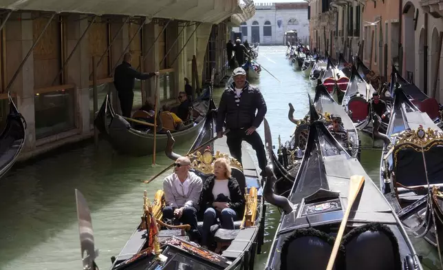 Tourists enjoy a ride on gondolas in Venice, Italy, Thursday, April 25, 2024. The fragile lagoon city of Venice begins a pilot program Thursday to charge daytrippers a 5 euro entry fee that authorities hope will discourage tourists from arriving on peak days. (AP Photo/Luca Bruno)