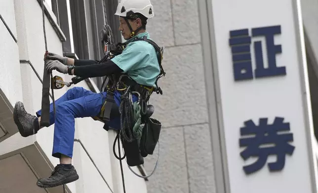 A window cleaner works along the window of at a securities firm building Tuesday, April 30, 2024, in Tokyo. Japanese characters read as "securities." (AP Photo/Eugene Hoshiko)
