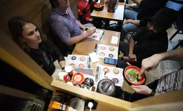 Frank Striegl, bottom right, a guide of Tokyo Ramen Tours, explains participants of a ramen tasting tour at Nagi, which offers "Fukuoka fusion," type ramen at Shibuya district on April 2, 2024, in Tokyo. (AP Photo/Eugene Hoshiko)