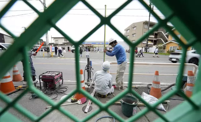 Workers set up a barricade near the Lawson convenience store, background, Tuesday, April 30, 2024, at Fujikawaguchiko town, Yamanashi Prefecture, central Japan. The town of Fujikawaguchiko, known for a number of popular photo spots for Japan's trademark of Mt. Fuji, on Tuesday began to set up a huge black screen on a stretch of sidewalk to block view of the mountain in a neighborhood hit by a latest case of overtourism in Japan. (AP Photo/Eugene Hoshiko)