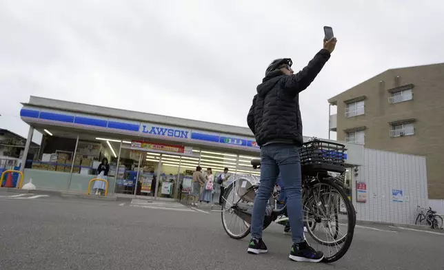 A tourist takes a selfie at the Lawson convenience store, a popular photo spot framing a picturesque view of Mt. Fuji in the background, on cloudy evening of Tuesday, April 30, 2024, at Fujikawaguchiko town, Yamanashi Prefecture, central Japan. The town of Fujikawaguchiko, known for a number of popular photo spots for Japan's trademark of Mt. Fuji, on Tuesday began to set up a huge black screen on a stretch of sidewalk to block view of the mountain in a neighborhood hit by a latest case of overtourism in Japan. (AP Photo/Eugene Hoshiko)