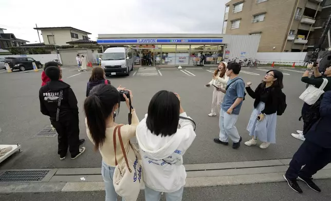 Tourists take pictures in front of the Lawson convenience store, a popular photo spot framing a picturesque view of Mt. Fuji in the background on cloudy evening of Tuesday, April 30, 2024, at Fujikawaguchiko town, Yamanashi Prefecture, central Japan. The town of Fujikawaguchiko, known for a number of popular photo spots for Japan's trademark of Mt. Fuji, on Tuesday began to set up a huge black screen on a stretch of sidewalk to block view of the mountain in a neighborhood hit by a latest case of overtourism in Japan. (AP Photo/Eugene Hoshiko)