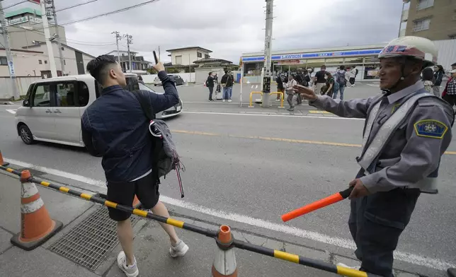 A security guard redirects a tourist outside of the construction site of a barricade near the Lawson convenience store Tuesday, April 30, 2024, at Fujikawaguchiko town, Yamanashi Prefecture, central Japan. The town of Fujikawaguchiko, known for a number of popular photo spots for Japan's trademark of Mt. Fuji, on Tuesday began to set up a huge black screen on a stretch of sidewalk to block view of the mountain in a neighborhood hit by a latest case of overtourism in Japan. (AP Photo/Eugene Hoshiko)
