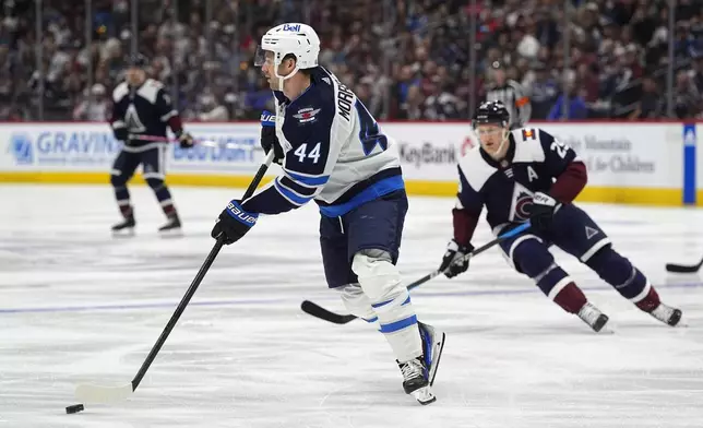 Winnipeg Jets defenseman Josh Morrissey (44) clears the puck as Colorado Avalanche center Nathan MacKinnon, right, defends in the first period of an NHL hockey game Saturday, April 13, 2024, in Denver. (AP Photo/David Zalubowski)