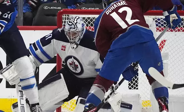 Winnipeg Jets goaltender Connor Hellebuyck, center, stops a shot by Colorado Avalanche right wing Brandon Duhaime (12) in the second period of Game 4 of an NHL Stanley Cup first-round playoff series Sunday, April 28, 2024, in Denver. (AP Photo/David Zalubowski)