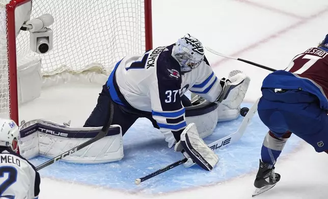 Winnipeg Jets goaltender Connor Hellebuyck, left, stops a shot from Colorado Avalanche center Casey Mittelstadt during the first period of Game 3 of an NHL hockey Stanley Cup first-round playoff series Friday, April 26, 2024, in Denver. (AP Photo/David Zalubowski)