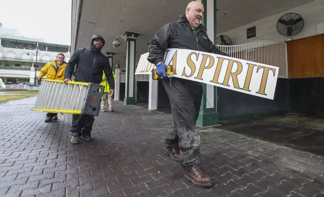 FILE - Todd Herl of the Churchill Downs sign shop carries the Medina Spirit sign after it was removed from the paddock at Churchill Downs Tuesday, Feb. 22, 2022, in Louisville, Ky. Trainer Bob Baffert will miss the race for the third consecutive year. He served a two-year suspension by Churchill Downs Inc. after his 2021 winner Medina Spirit was disqualified for a failed drug test. But the track’s corporate ownership meted out an additional year of punishment. Michael Clevenger/Courier Journal via AP, File)