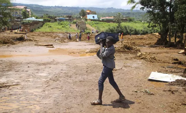 A child carrying a suitcase, walks, after a dam burst, in Kamuchiri Village Mai Mahiu, Nakuru County, Kenya, Monday, April 29, 2024. Police in Kenya say at least 40 people have died after a dam collapsed in the country's west. (AP Photo/Patrick Ngugi)
