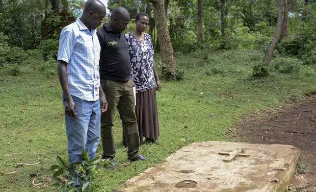 Humphrey Kizito, centre, with his brother and sister in law, stand by their parents gravesite at their home in Siaya, Kenya Saturday, April. 13, 2024. Even after parts of Kenya participated in an important pilot of the world's first malaria vaccine, with a reported drop in deaths for children under 5, the disease is still a significant public health challenge. Kenya's health ministry hasn't said when the vaccine will be widely available. (AP Photo/Brian Ongoro)