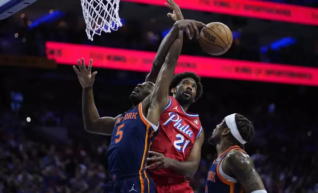 Philadelphia 76ers' Joel Embiid, center, reaches over New York Knicks' Precious Achiuwa, left, for a rebound during the first half of Game 4 in an NBA basketball first-round playoff series, Sunday, April 28, 2024, in Philadelphia. (AP Photo/Matt Slocum)