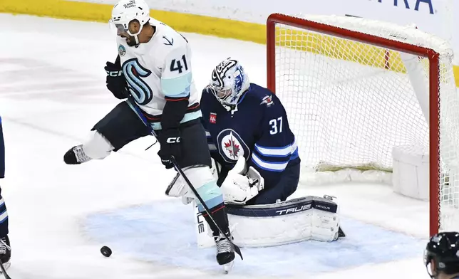 Seattle Kraken's Pierre-Edouard Bellmare (41) jumps out of the way as a puck is shot on Winnipeg Jets goaltender Connor Hellebuyck (37) during the first period of an NHL hockey game in Winnipeg, Manitoba on Tuesday April 16, 2024. (Fred Greenslade/The Canadian Press via AP)