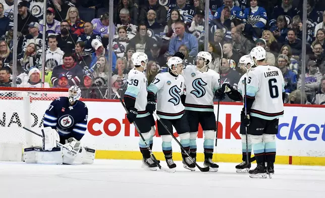 Seattle Kraken's Tye Kartye (52) celebrates his goal on Winnipeg Jets goaltender Connor Hellebuyck (37) with teammates during the second period of an NHL hockey game in Winnipeg, Manitoba on Tuesday April 16, 2024. (Fred Greenslade/The Canadian Press via AP)