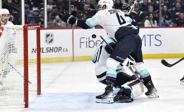 Seattle Kraken's Justin Schultz (4) reaches for a loose puck behind goaltender Philipp Grubauer (31) after a shot by the Winnipeg Jets during the second period of an NHL hockey game in Winnipeg, Manitoba on Tuesday April 16, 2024. (Fred Greenslade/The Canadian Press via AP)