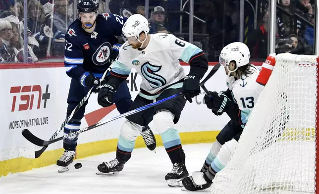 Seattle Kraken's Adam Larsson (6) and Brandon Tanev (13) battle for the puck against Winnipeg Jets' Mason Appleton (22) during the second period of an NHL hockey game in Winnipeg, Manitoba on Tuesday April 16, 2024. (Fred Greenslade/The Canadian Press via AP)