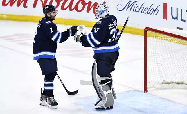 Winnipeg Jets' goaltender Connor Hellebuyck (37) celebrates the win over the Seattle Kraken with Dylan DeMelo (2) after an NHL hockey game in Winnipeg, Manitoba on Tuesday April 16, 2024. (Fred Greenslade/The Canadian Press via AP)