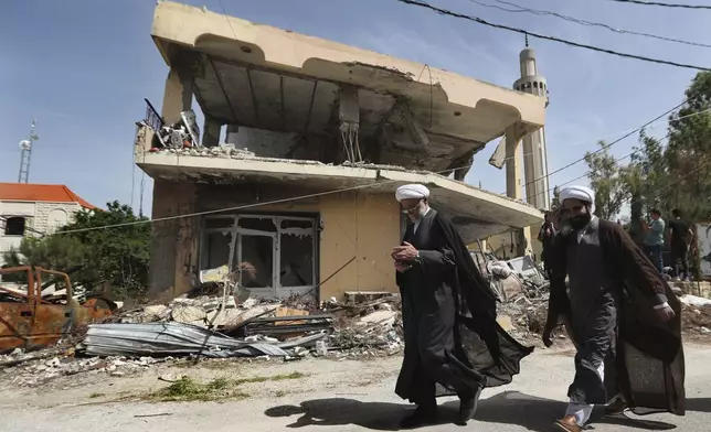 Shiite clerics pass in front of a house that was destroyed by an Israeli airstrike, in Hanine village, south Lebanon, Thursday, April 25, 2024. Hezbollah militants and Israeli forces have been exchanging fire since a day after the Israel-Hamas war began on Oct. 7. (AP Photo/Mohammed Zaatari)