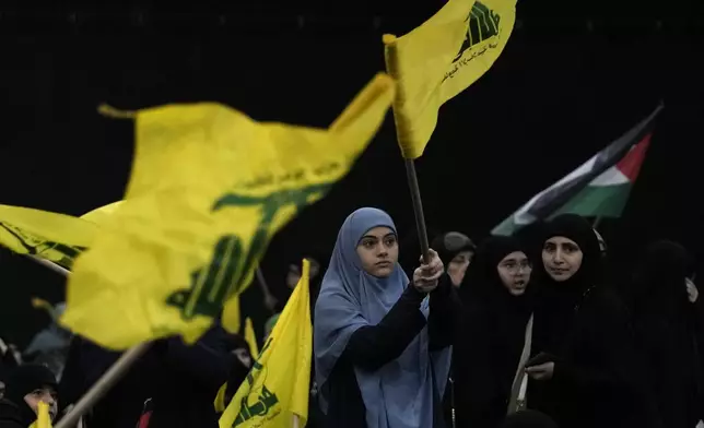 Hezbollah supporters wave Hezbollah and Palestinian flags as Hezbollah leader Sayyed Hassan Nasrallah speaks via a video link during a ceremony to commemorate the death of the Iranian Revolutionary Guard Gen. Mohammad Reza Zahedi, and six officers, who were killed by an Israeli airstrike that demolished Iran's consulate in Syria last Monday, in the southern suburbs of Beirut, Lebanon, Monday, April 8, 2024. Nasrallah paid tribute to Zahedi, who spent 12 years of his career as a top general at the Iranian Revolutionary Guards elite Quds Force with Hezbollah. The Hezbollah leader said he played a key role in strengthening and empowering the group which fought several wars with Israel, and has become Iran's key proxy in the region. (AP Photo/Hassan Ammar)
