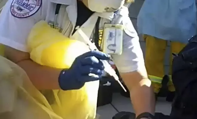 In this image from Colorado Springs Police Department body-camera video, a paramedic prepares to inject ketamine as police restrain Hunter Barr outside his father's home in Colorado Springs, Colo., on Sept. 25, 2020. Retired postal worker Mark Barr had called 911 for help controlling his son, who he said wasn't violent but was having a bad reaction to LSD. He watched as a medic gave two injections. His son was dead within hours. "I couldn't figure out why that was necessary," he said of the second injection. (Colorado Springs Police Department via AP)