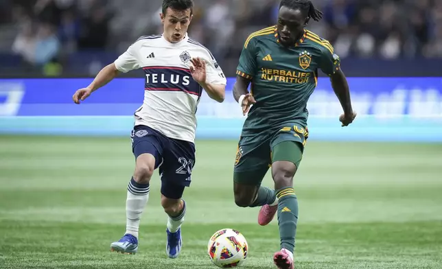 Vancouver Whitecaps' Andres Cubas, left, and LA Galaxy's Joseph Paintsil vie for the ball during the first half of an MLS soccer match Saturday, April 13, 2024, in Vancouver, British Columbia. (Darryl Dyck/The Canadian Press via AP)