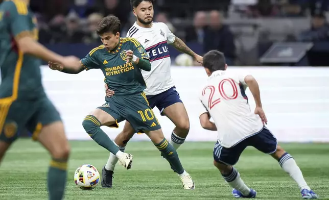 LA Galaxy's Riqui Puig (10) evades Vancouver Whitecaps' Ryan Raposo, back, and Andres Cubas (20) during the first half of an MLS soccer match Saturday, April 13, 2024, in Vancouver, British Columbia. (Darryl Dyck/The Canadian Press via AP)