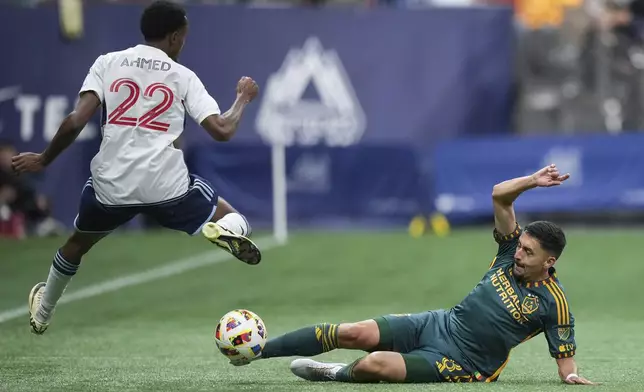 LA Galaxy's Mark Delgado, right, slides to take the ball away from Vancouver Whitecaps' Ali Ahmed during the first half of an MLS soccer match Saturday, April 13, 2024, in Vancouver, British Columbia. (Darryl Dyck/The Canadian Press via AP)