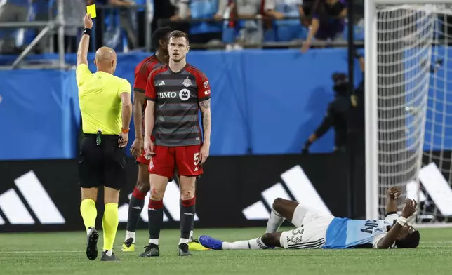 Referee Allen Chapman, left, shows a yellow card to Toronto FC defender Kevin Long (5) as Charlotte FC forward Patrick Agyemang lies on the field during the second half of an MLS soccer match in Charlotte, N.C., Saturday, April 13, 2024. (AP Photo/Nell Redmond)