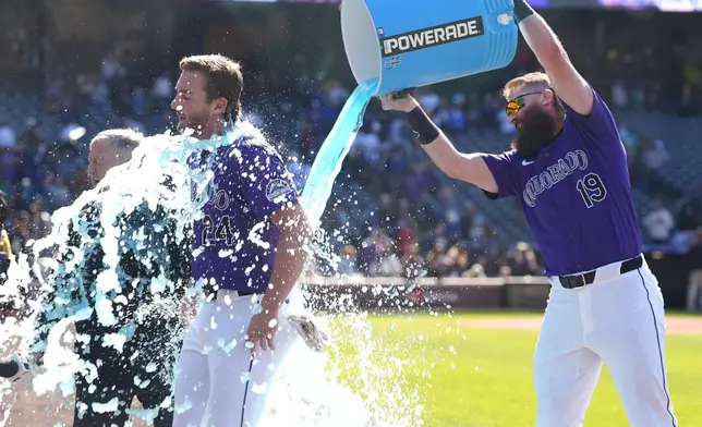 Colorado Rockies' Ryan McMahon, left, is doused by teammate Charlie Blackmon (19) as McMahon is interviewed after hitting a walk-off RBI single in the 10th inning of the first game of a baseball doubleheader against the Seattle Mariners Sunday, April 21, 2024, in Denver. (AP Photo/David Zalubowski)