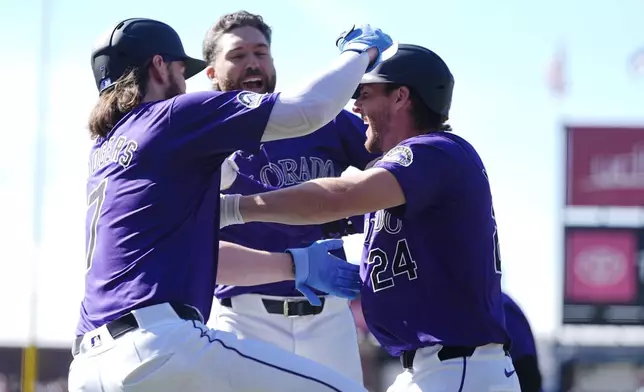 Colorado Rockies' Brendan Rodgers, left, and Jake Cave, center, congratulate Ryan McMahon after his RBI single to drive in the winning run in the 10th inning of the first game of a baseball doubleheader against the Seattle Mariners, Sunday, April 21, 2024, in Denver. (AP Photo/David Zalubowski)