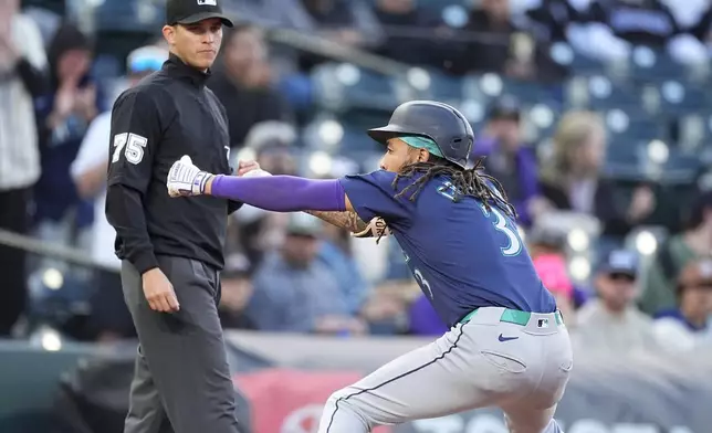 Seattle Mariners' J.P. Crawford, right, celebrates after tripling to drive in three runs as third base umpire Tom Woodring, left, looks on in the second inning of the second game of a baseball doubleheader against the Colorado Rockies, Sunday, April 21, 2024, in Denver. (AP Photo/David Zalubowski)