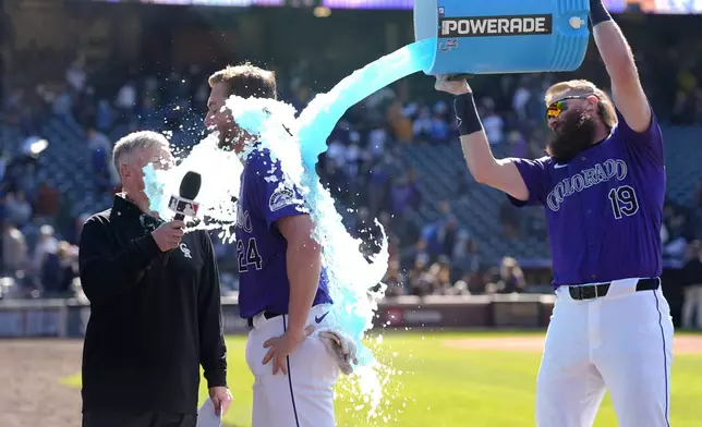 Colorado Rockies' Ryan McMahon, center, is doused by teammate Charlie Blackmon, right, while being interviewed by Marc Stout after McMahon hit a walk-off RBI single in the 10th inning of the first game of a baseball doubleheader against the Seattle Mariners Sunday, April 21, 2024, in Denver. (AP Photo/David Zalubowski)
