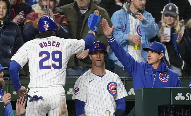 Chicago Cubs' Michael Busch is greeted at the dugout by manager Craig Counsell, right, and Yan Gomes after Busch scored against the Miami Marlins during the sixth inning in the second baseball game of a doubleheader Saturday, April 20, 2024, in Chicago. (AP Photo/Charles Rex Arbogast)