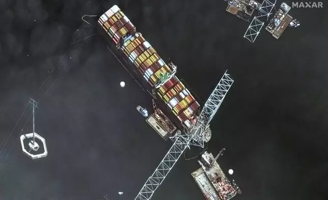 This satellite image provided by Maxar shows the bow of the container ship Dali remains stuck underneath sections of the fallen Francis Scott Key Bridge, while salvage crews and barges with cranes continue removing some of the bridge debris and hundreds of shipping containers still onboard the vessel, in Baltimore, Monday, April 8, 2024. (Satellite image ©2024 Maxar Technologies via AP)