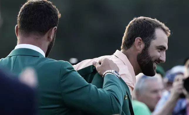 Jon Rahm, of Spain, puts the green jacket on winner Scottie Scheffler after the Masters golf tournament at Augusta National Golf Club Sunday, April 14, 2024, in Augusta, Ga. (AP Photo/Charlie Riedel)