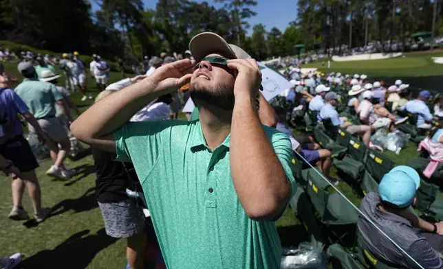 A patron looks up at the sun during an solar eclipse during a practice round in preparation for the Masters golf tournament at Augusta National Golf Club Monday, April 8, 2024, in Augusta, Ga. (AP Photo/Ashley Landis)