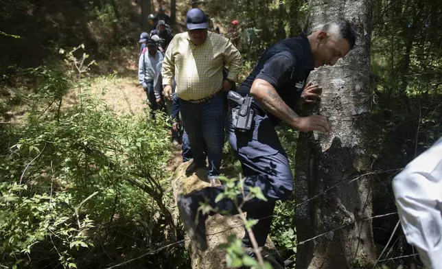An armed police officer accompanies locals from Villa Madero through the mountains in search of unlicensed water intakes and irrigation ponds during a drought in Villa Madero, Mexico, Wednesday, April 17, 2024. Subsistence farmers and activists from the Michoacan town of Villa Madero organized teams to go into the mountains and rip out illegal water pumps and breach unlicensed irrigation holding ponds. (AP Photo/Armando Solis)