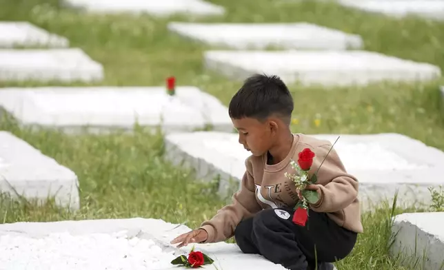 A boy lays flowers on a grave at the cemetery in Kato Tritos village on the northeastern Aegean Sea island of Lesbos, Greece, on Wednesday, April 17, 2024. After years of neglect, a primitive burial ground for refugees who died trying to reach Greece's island of Lesbos has been cleaned up and redesigned to provide a dignified resting place for the dead. (AP Photo/Panagiotis Balaskas)