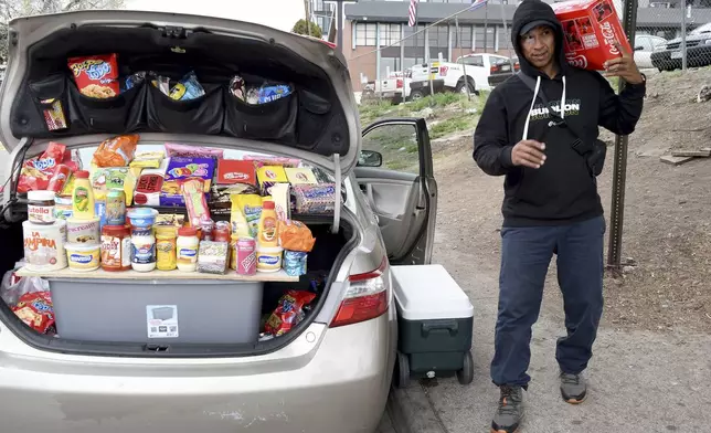 Alvaro Machado sells packaged food brands from South America out of the back of his car outside a motel designated for migrants in Denver, Colorado, Thursday, April 18, 2024. Machado, from Venezuela, said he came to Denver six months ago. (AP Photo/Thomas Peipert)