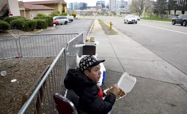 Lincoln Montero eats outside a motel designated for migrants after helping his aunt Yesenia sell home-cooked Venezuelan-style food to fellow Venezuelan migrants sheltering here in Denver, Colorado, Thursday, April 18, 2024. Montero said he traveled to Denver the week before, to unite with his aunt who has been here four months. (AP Photo/Thomas Peipert)