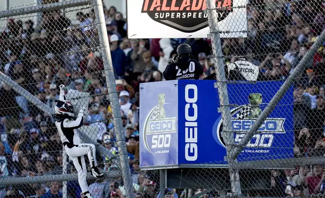 Tyler Reddick celebrates his win and climbs a fence at a NASCAR Cup Series auto race at Talladega Superspeedway, Sunday, April 21, 2024, in Talladega. Ala. (AP Photo/Mike Stewart)