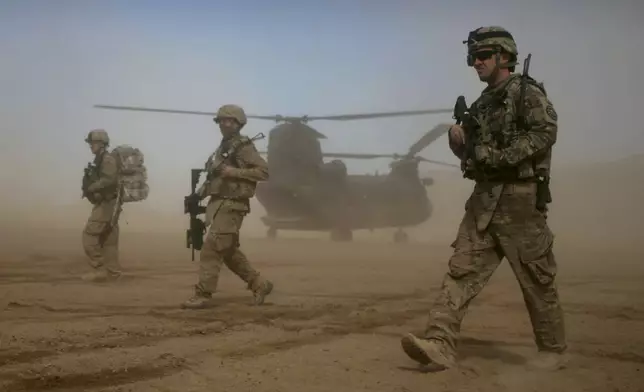 FILE - U.S. soldiers, part of the NATO- led International Security Assistance Force (ISAF), walk as a U.S. Chinook helicopter is seen on the back ground in Shindand, Herat, west of Kabul, Afghanistan, Saturday, Jan. 28, 2012. NATO is set to celebrate on Thursday, April 4, 2024, 75 years of collective defense across Europe and North America as Russia's war on Ukraine enters its third year. (AP Photo/Hoshang Hashimi, File)