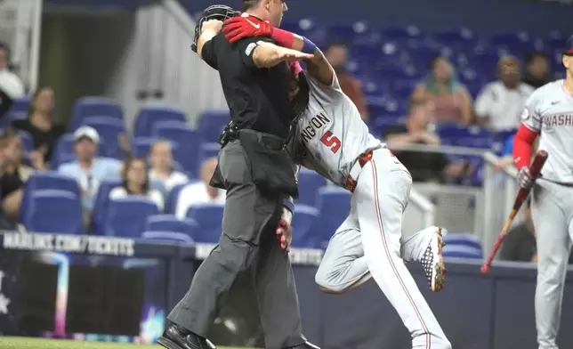 Washington Nationals' CJ Abrams (5) runs into the home plate umpire as he scores on a wild throw by Miami Marlins pitcher Andrew Nardi during the seventh inning of a baseball game, Monday, April 29, 2024, in Miami. (AP Photo/Lynne Sladky)